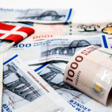 Danske pengesedler spredt ud med et lille dansk flag, herunder 500- og 1000-kronesedler.