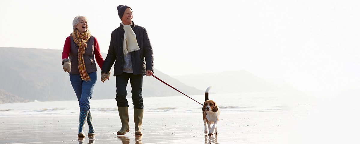 En person går med en hund i snor langs en strand på en overskyet dag.