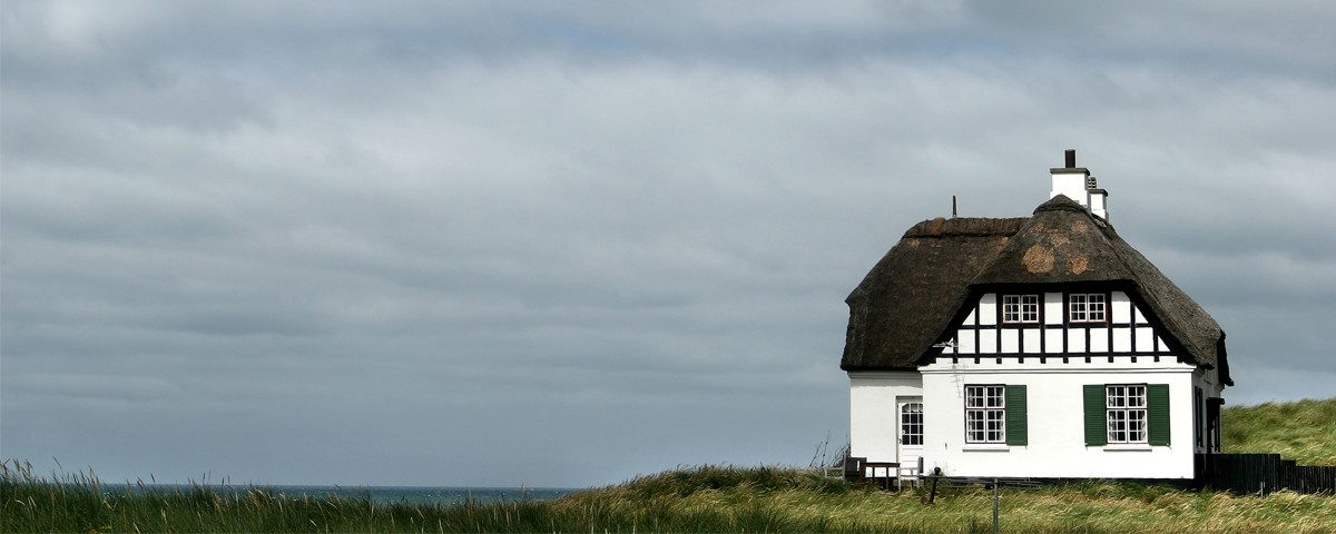 Et hvidt hus med stråtag beliggende på en græsmark under en overskyet himmel.