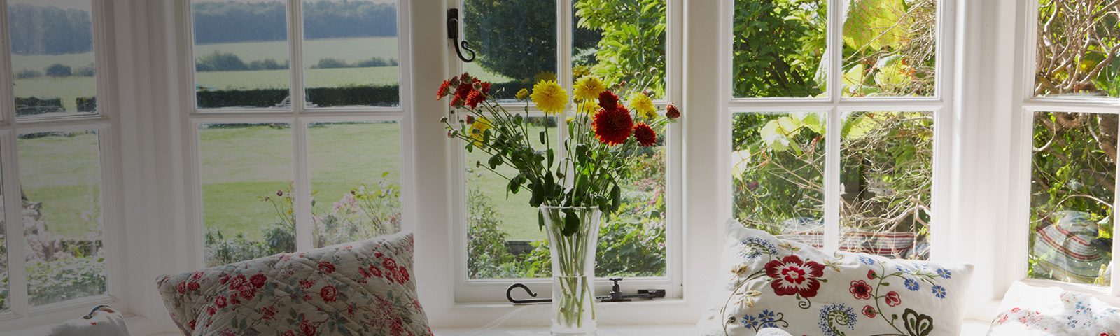En glasvase med farverige blomster, placeret på en vindueskarm med udsigt til en have.