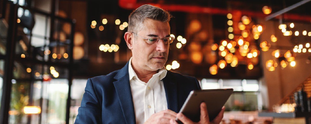 En mand i jakkesæt kigger koncentreret på en tablet i et varmt oplyst miljø.