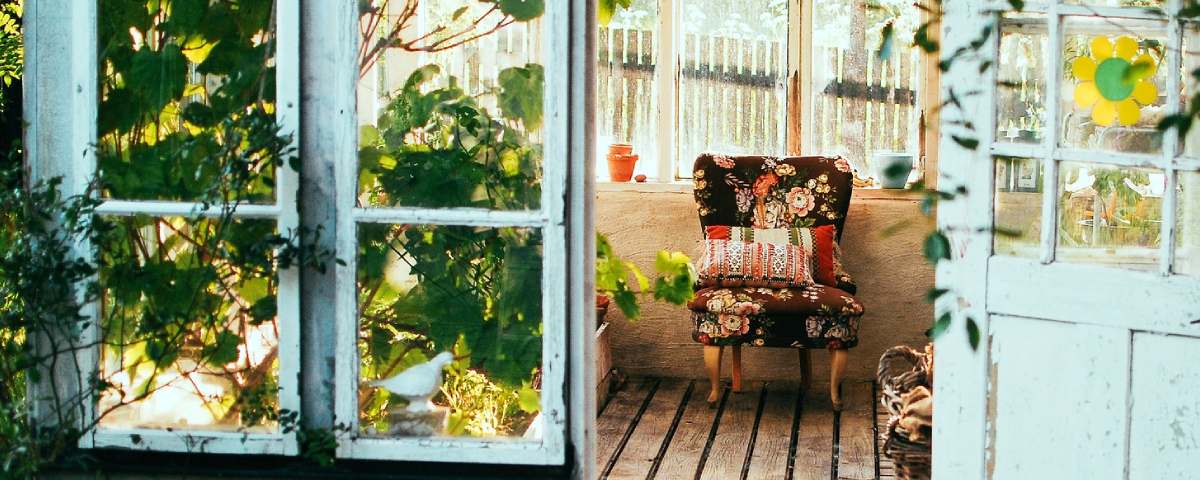 En stol med blomsterprint står i et lyst drivhus omgivet af grønne planter.