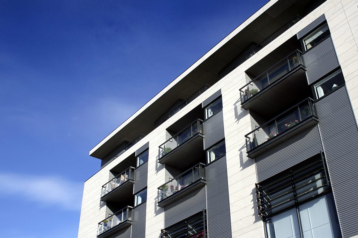 En moderne bygning med balkoner på hver etage under en klar blå himmel.
