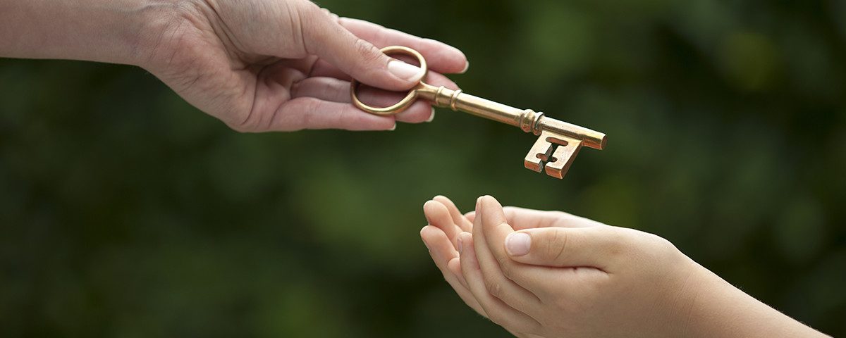En hånd rækker en gammeldags nøgle til en anden persons åbne hænder foran en grøn baggrund.