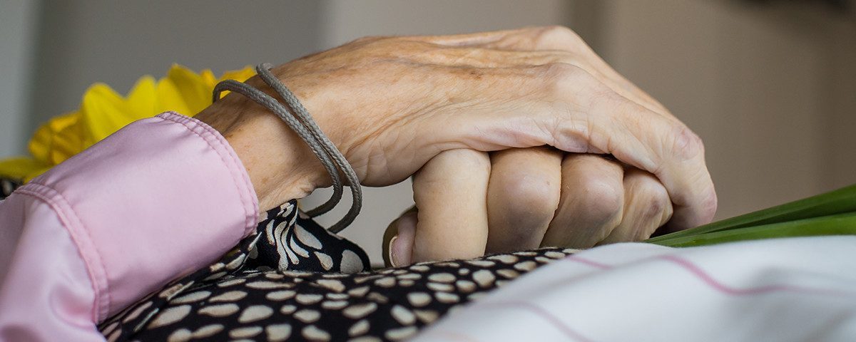 To hænder holder hinanden; den ene er ældre med en armbåndssnor, den anden er yngre.