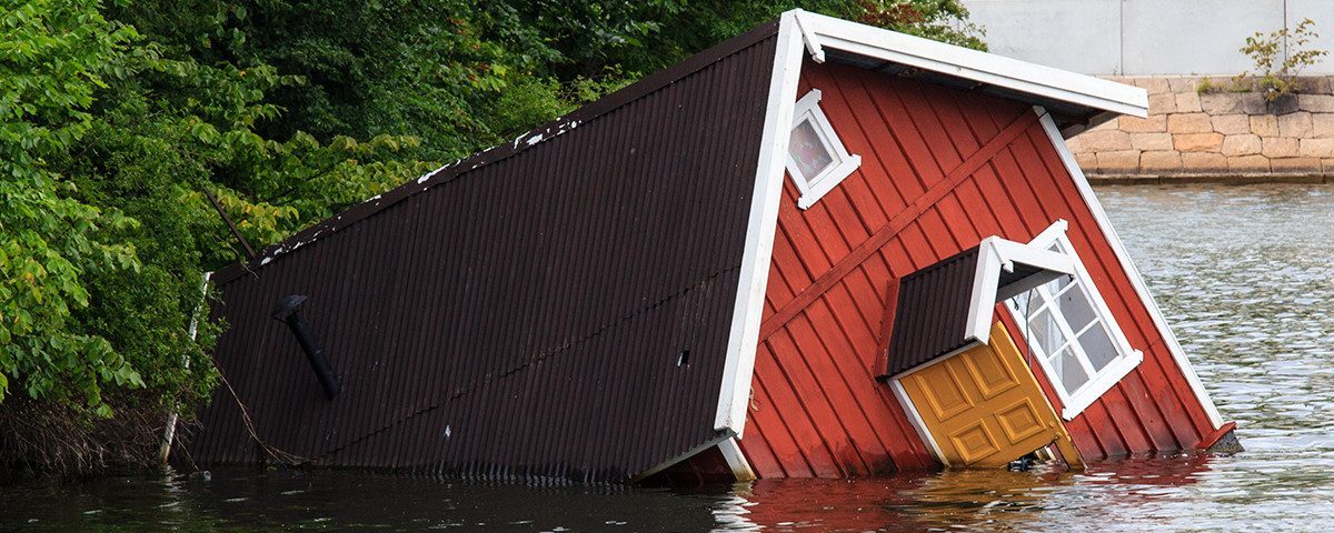Et rødt hus med mørkt tag ligger halvt nedsunket i vand.