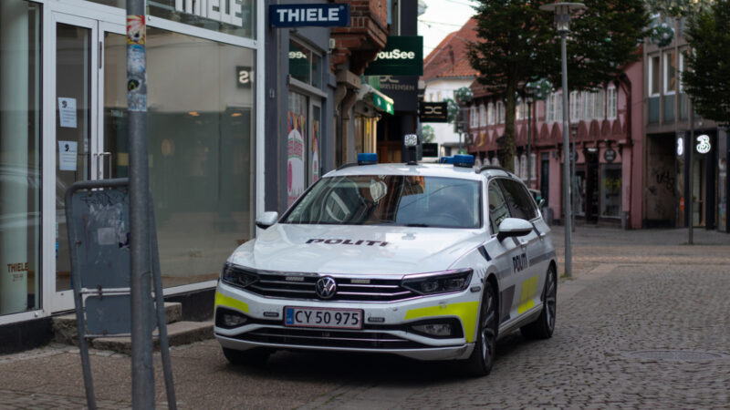En politibil parkeret på en brostensbelagt gade foran en butik med skiltet