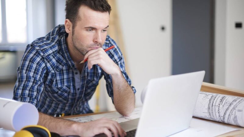 Mand ved computer, hvor der ligger høreværn og byggeplaner ved siden af