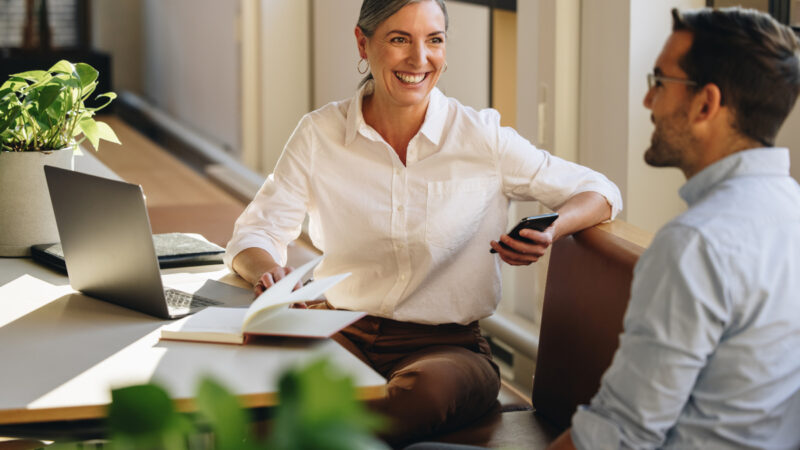 Kvinde og mand sidder på kontor ved en computer og snakker