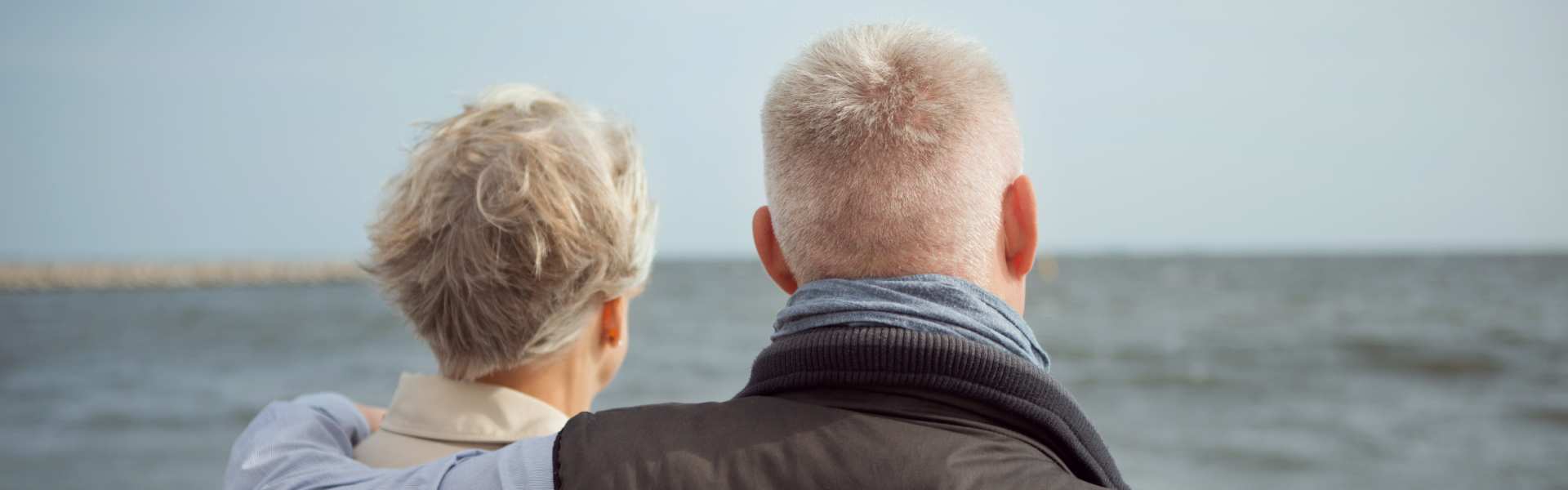 Modent par med gråt hår står med ryggen til og kigger udover vandet